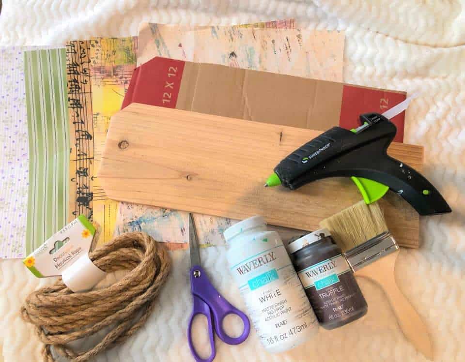 Supplies needed for a diy floral banner including wood, rope, glue gun, paint, scrapbook paper