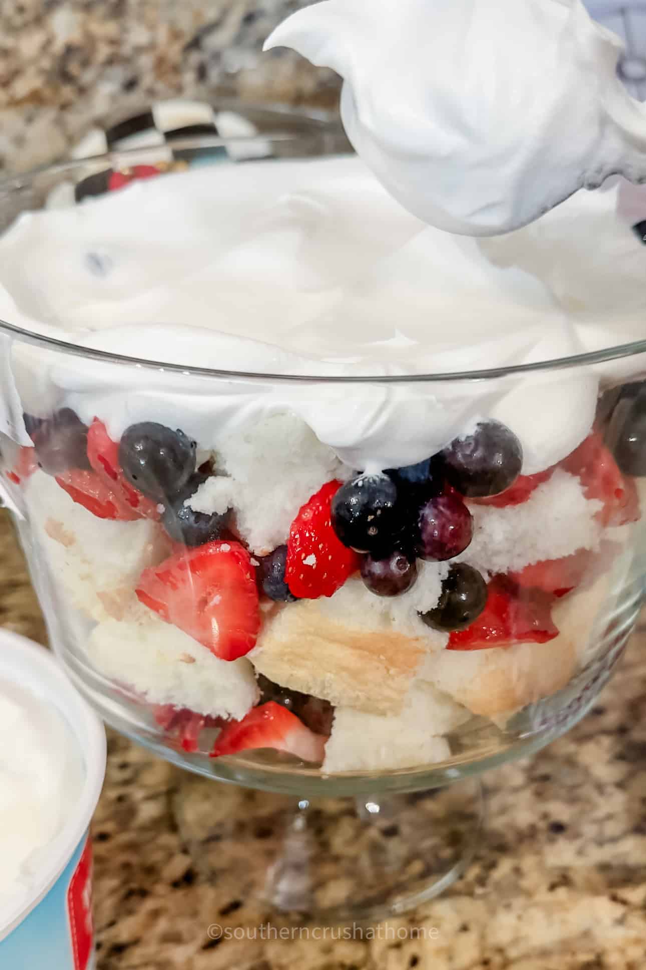 adding top layer of whipped cream to blueberry strawberry trifle