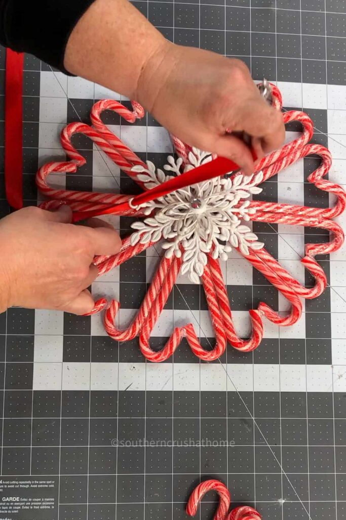 tying a red satin ribbon to a candy cane wreath